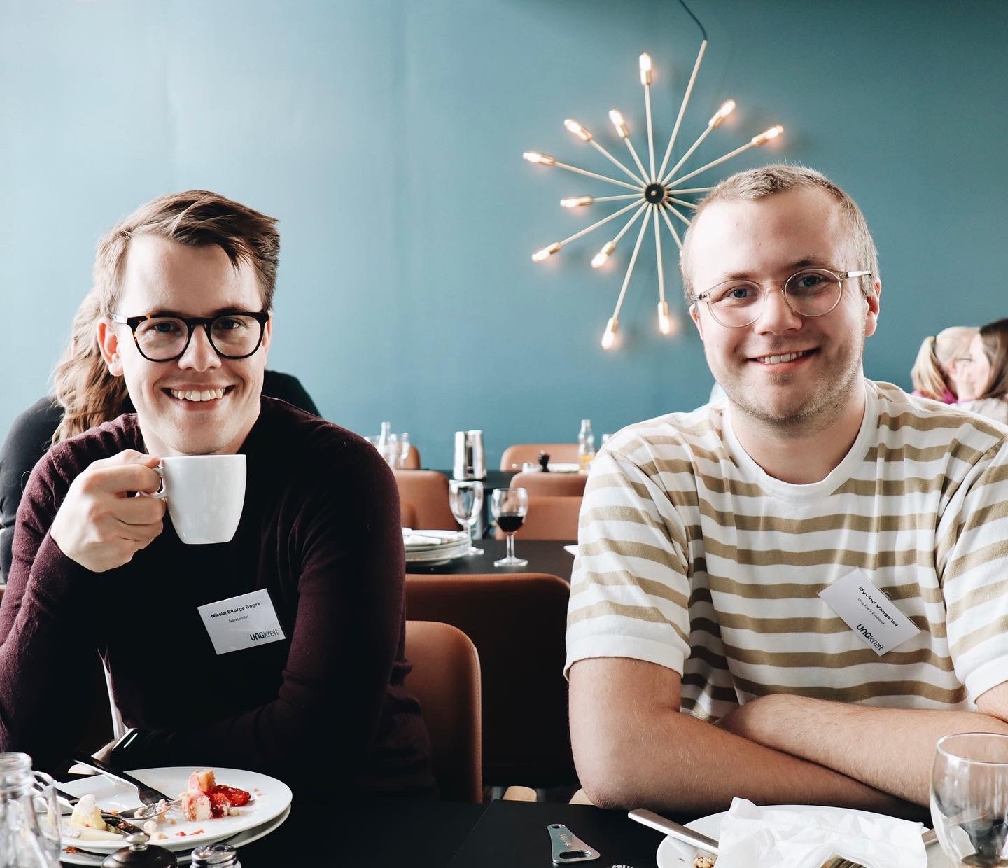 To menn spiser frokost ved et bord mens de smiler inn i kamera