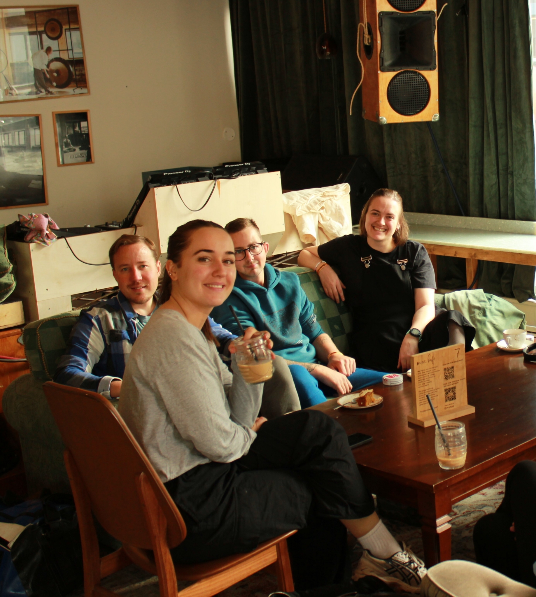 Unge personer sitter i sofaer ved et kafébord og smiler til kamera