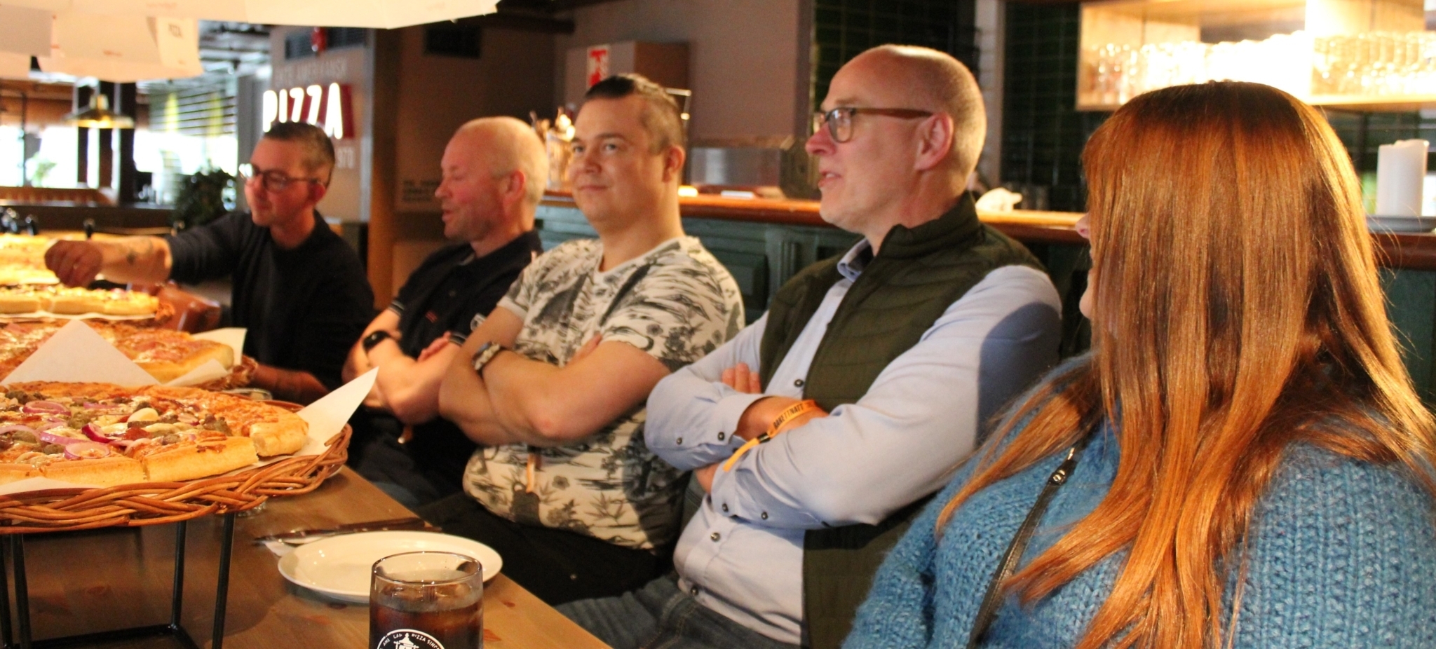 Fem personer sitter langs et bord fylt av pizza