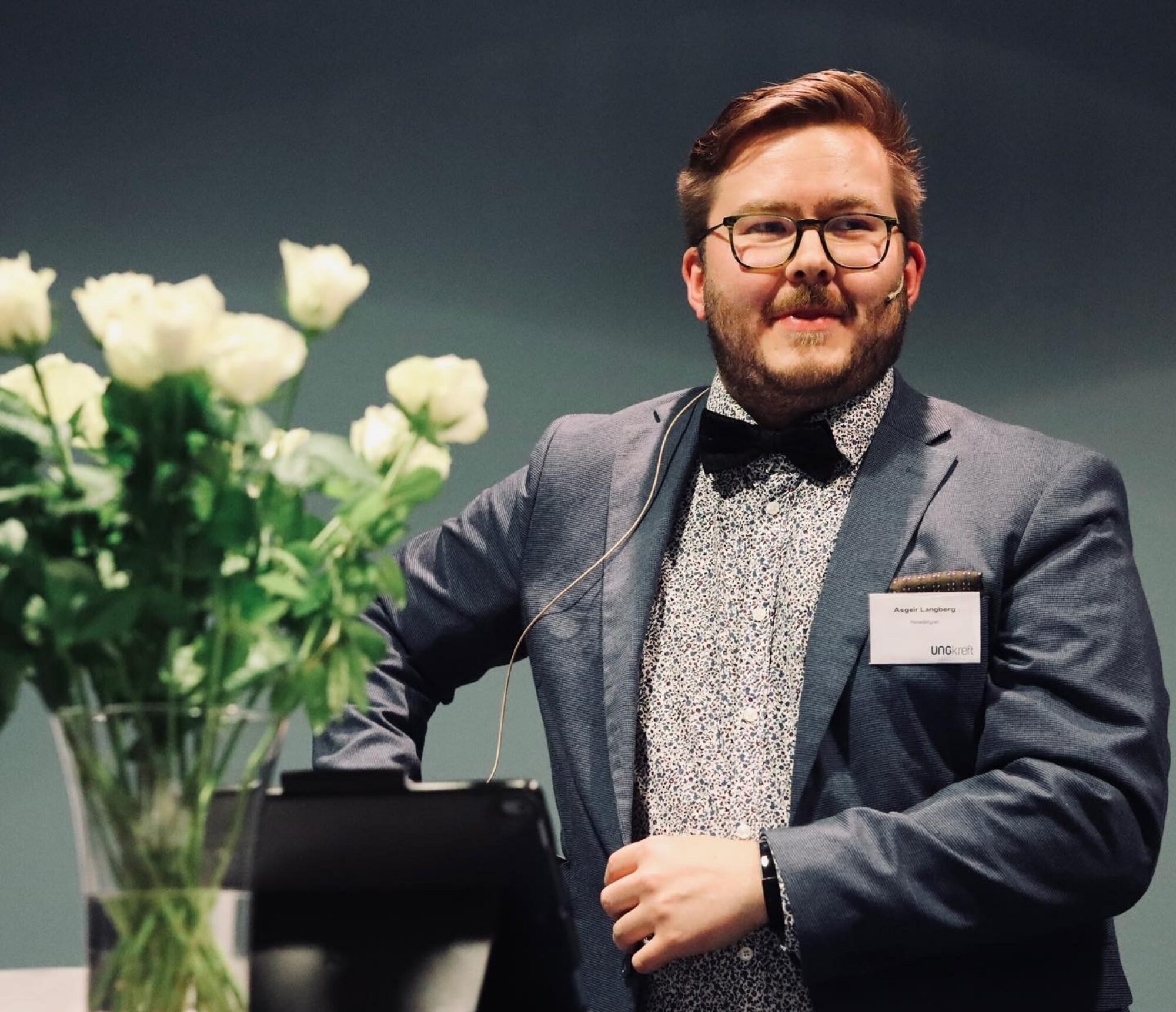 Styreleder Asgeir står i pendress på talerstolen med blomster ved siden av seg