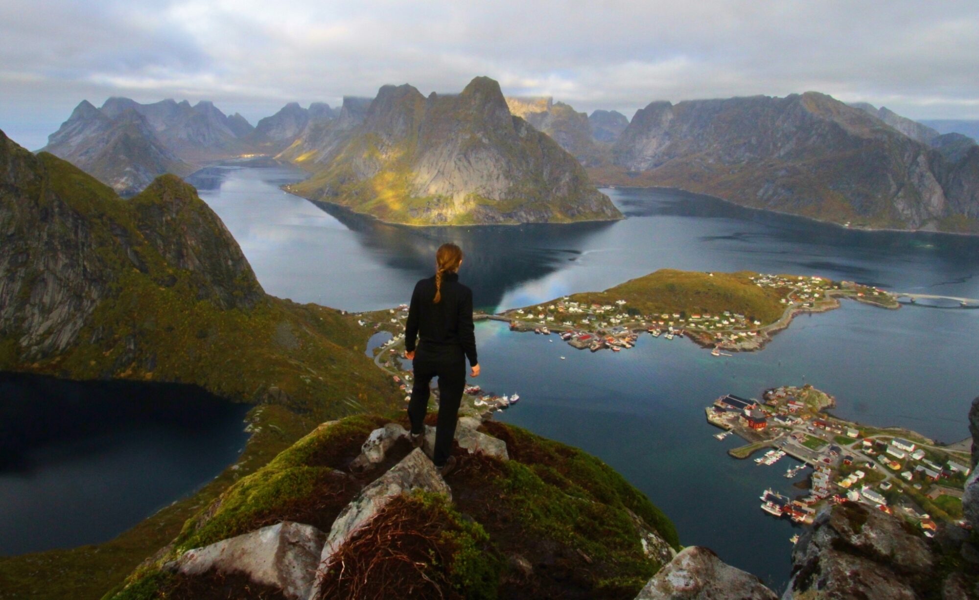 Karoline står på toppen av et fjell og ser utover sjø og fjell.