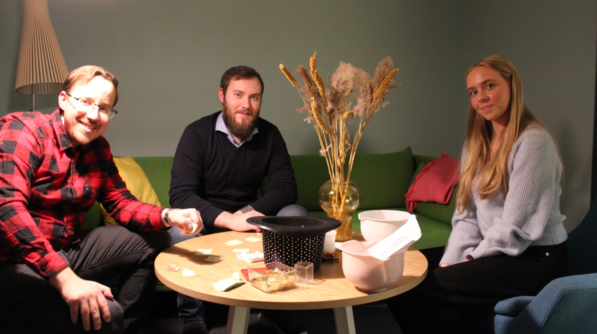 To gutter og en jente sitter rundt et bord fylt av papirkapper og en flosshatt med åpningen opp