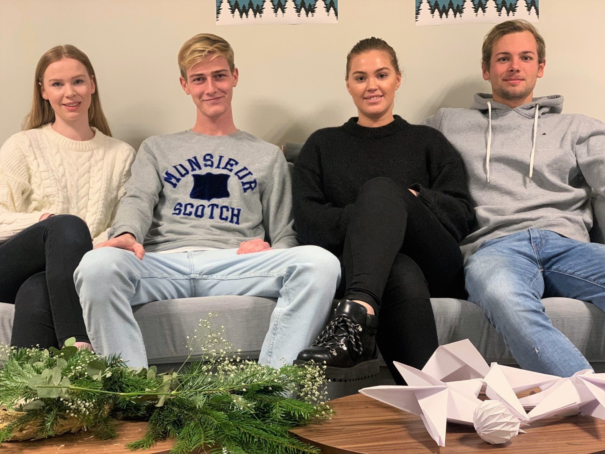 Fire studenter sitter i en sofa med julepynt på bordet foran seg