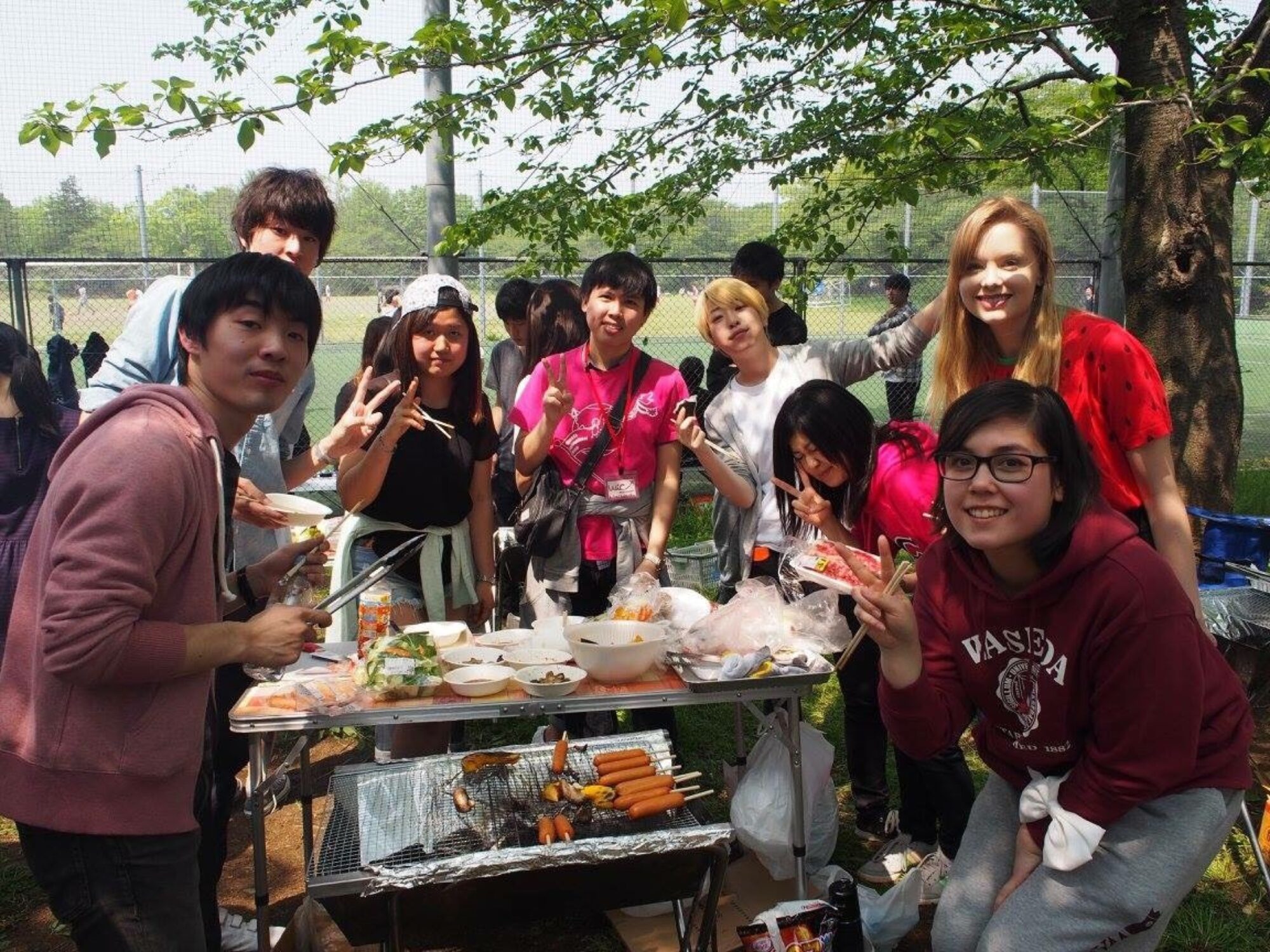 Studenter står rundt et bord med mat ute i naturen. De smiler inn i kamera.