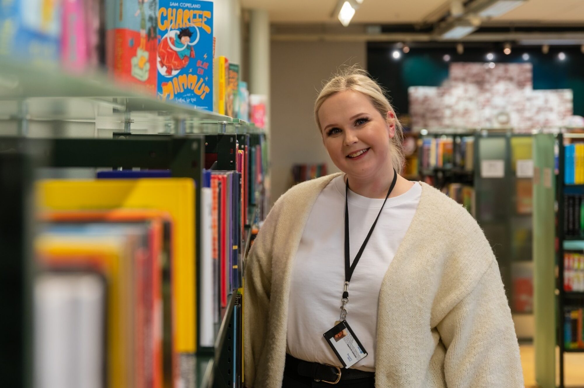 Vilde står på biblioteket og smiler inn i kameraet. Ved siden av henne står en lang reol med bøker.